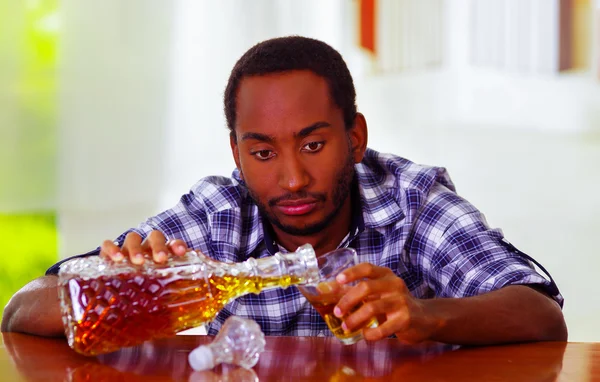 Handsome man wearing white blue shirt sitting by bar counter lying over desk pouring drink from decanter into glass, drunk depressed facial expression, alcoholic concept — Stock Photo, Image