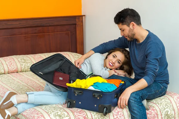 Jeune couple hispanique charmant portant des vêtements décontractés assis sur le lit emballage dans la valise ensemble, concept d'invité auberge — Photo