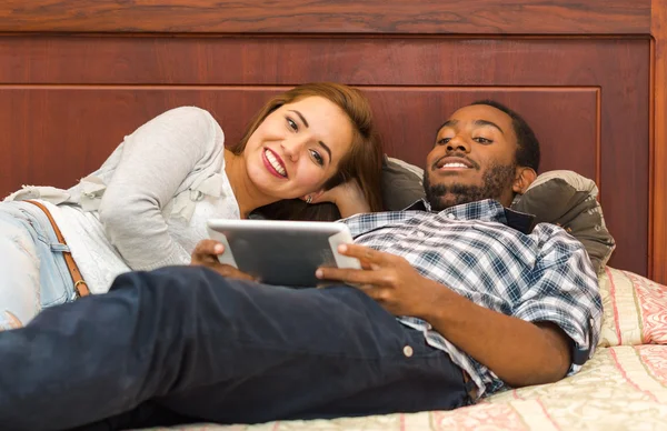 Affascinante giovane coppia sdraiata sul letto indossando abiti casual, felicemente guardando schermo tablet, concetto ostello ospite — Foto Stock