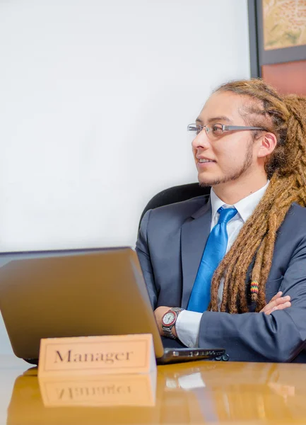 Handsome man with dreads and business suit sitting by desk, arms crossed, young manager concept — Stock Photo, Image