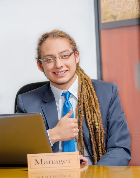 Handsome man with dreads and business suit sitting by desk looking at camera giving thumb up, young manager concept — Stock Photo, Image