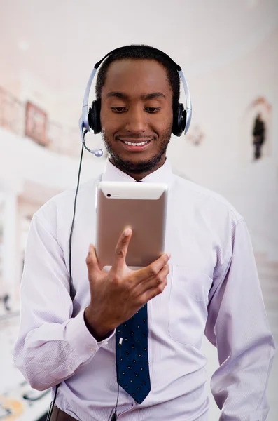 Handsome man wearing headphones with microphone, white striped shirt and tie, posing holding tablet in hand, smiling interacting — Stock Photo, Image