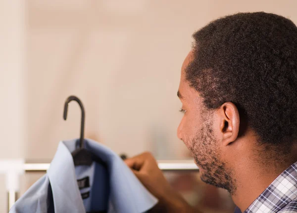 Headshot young man from behind, standing in front of clothing rack looking at blue shirt, fashion concept