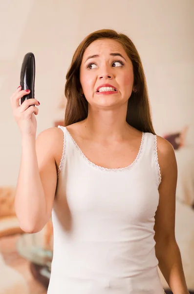 Young attractive woman wearing white top facing camera while talking on phone, holding up telephone showing dissatisfying facial expression — Stock Photo, Image