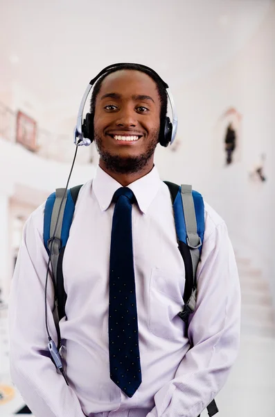 Beau homme portant des écouteurs avec microphone, sac à dos, chemise à rayures blanches et cravate souriante à la caméra, concept d'entreprise — Photo