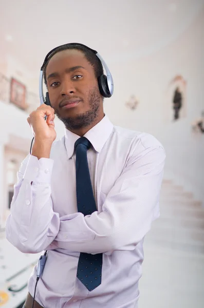 Pohledný muž, který nosí sluchátka s mikrofonem, bílou pruhovanou košili a kravatu a představuje interakci pro kameru — Stock fotografie