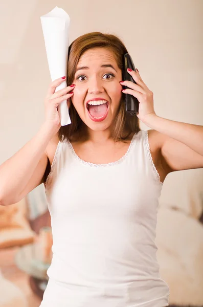 Jovem mulher vestindo câmera virada para cima branco enquanto gritando de frustração, segurando papel e telefone celular, conceito estressado — Fotografia de Stock