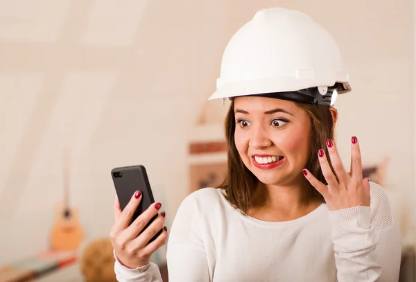 Jeune femme portant un casque de construction regardant le téléphone portable avec expression faciale stressée — Photo