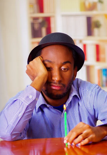 Affascinante uomo che indossa camicia blu e cappello seduto al tavolo con una candela cercando depresso, celebrando da solo — Foto Stock