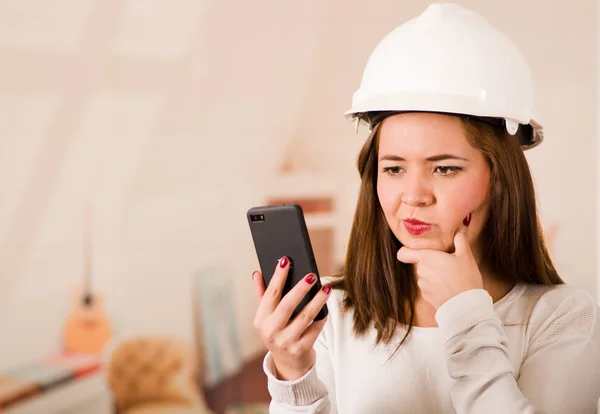 Jeune femme portant un casque de construction regardant le téléphone portable avec expression faciale stressée — Photo