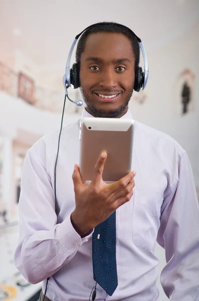 Handsome man wearing headphones with microphone, white striped shirt and tie, posing holding tablet in hand, smiling interacting — Stock Photo, Image