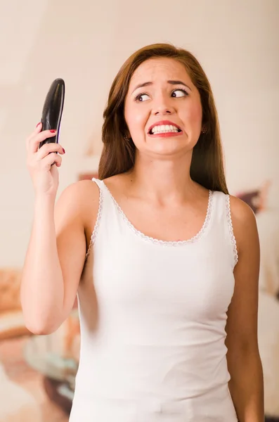 Молодая привлекательная женщина, одетая в белую верхнюю камеру, разговаривая по телефону, держа телефон, показывая неудовлетворяющее выражение лица — стоковое фото