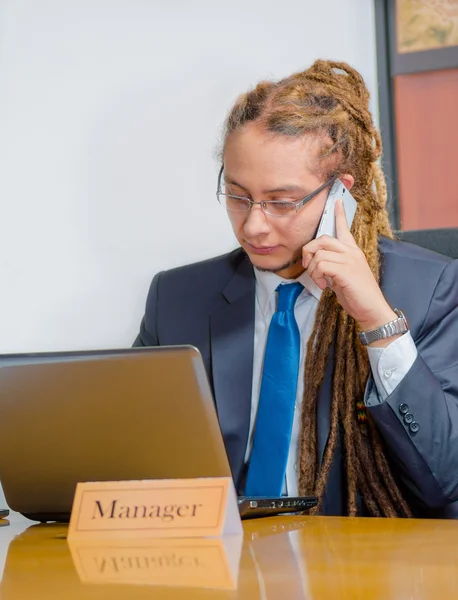 Przystojny mężczyzna z dredy i garniturze, siedząc przy biurku rozmowy na telefon komórkowy, koncepcja młody Menedżer — Zdjęcie stockowe