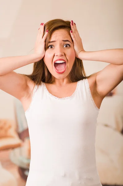 Mujer joven con la parte superior blanca frente a la cámara mientras grita en la frustración, concepto de estrés —  Fotos de Stock