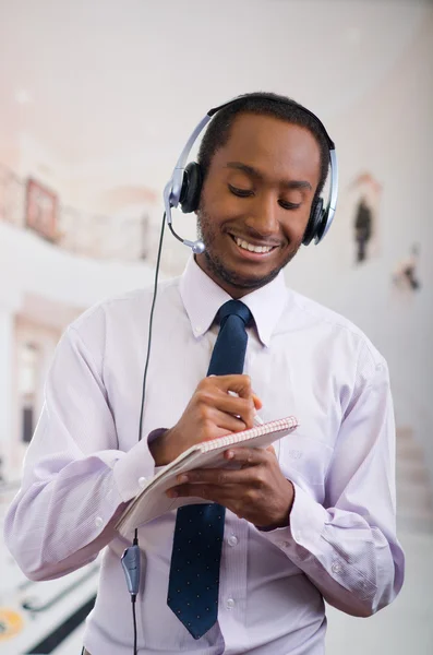 Handsome man wearing headphones with microphone, white striped shirt and tie, posing holding notebook in hand, smiling interacting — Stock Photo, Image