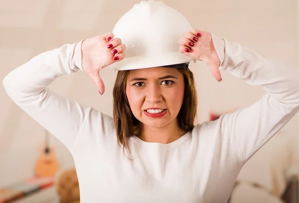 Young woman wearing construction helmet facing camera looking frustrated, upset body language giving thumbs down — Stock Photo, Image