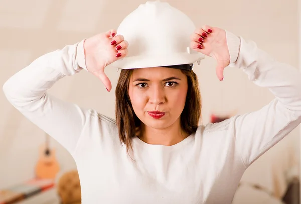 Young woman wearing construction helmet facing camera looking frustrated, upset body language giving thumbs down — Stock Photo, Image