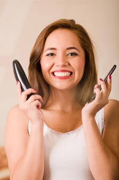 Mujer atractiva joven con la parte superior blanca frente a la cámara mientras habla en dos teléfonos sonriendo — Foto de Stock