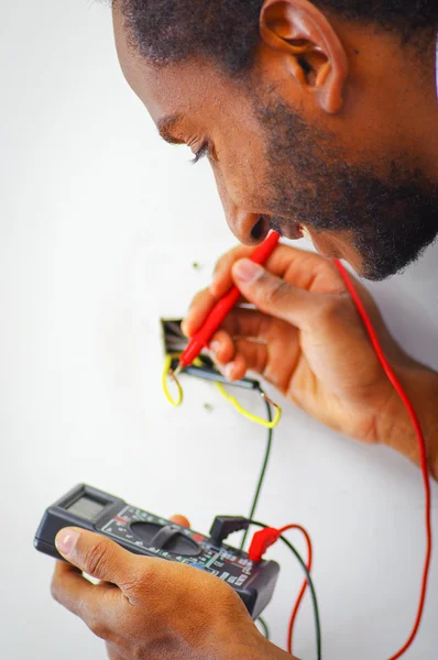 Чоловік у біло-блакитній сорочці, що працює на дротах електричних настінних гнізд, використовуючи мультиметр, концепція електрика — стокове фото