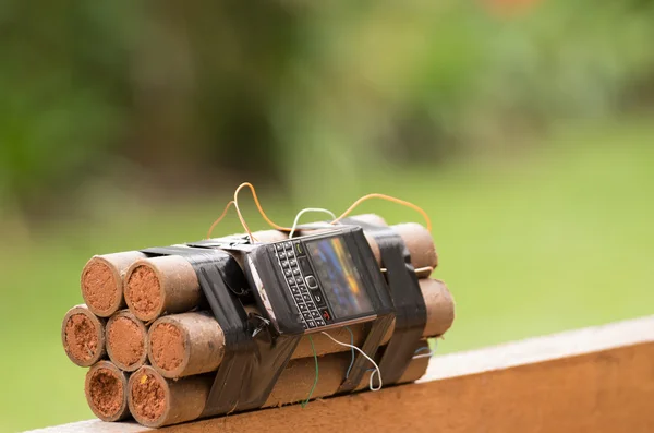 Самодельная бомба со взрывчаткой и сотовым телефоном прикреплены провода сидя на деревянной поверхности, зеленый сад на заднем плане — стоковое фото