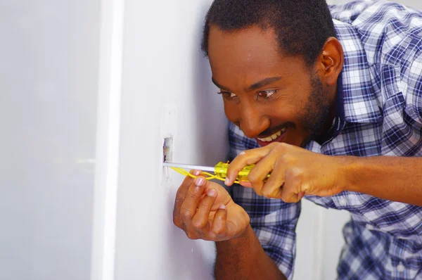 Hombre con camisa blanca y azul trabajando en cables de enchufe de pared eléctricos usando destornillador, expresión facial concentrada — Foto de Stock