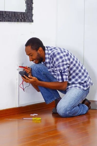 Man met witte en blauwe shirt werkt op elektrische muur aansluiting draden met behulp van multimeter, elektricien concept — Stockfoto