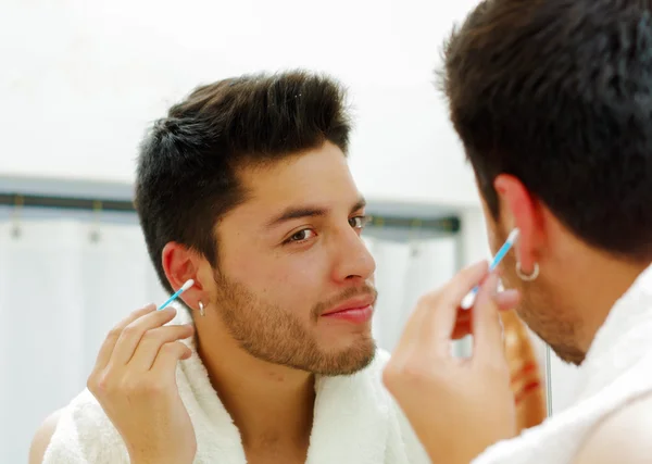 Beau jeune homme portant un haut singulet noir regardant dans un miroir, en utilisant q-tip pendant le concept de routine du matin — Photo