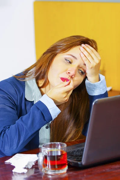 Mulher jovem doente de gripe, sentada à mesa usando o computador trabalhando, olhando mal e cansado, medicamentos, tecidos, vidro de água na mesa — Fotografia de Stock