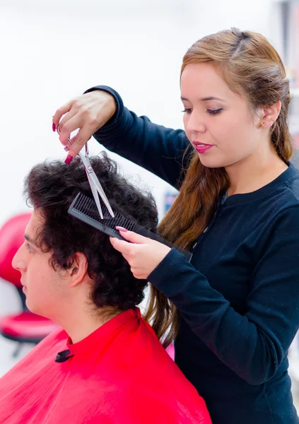 El pelo rizado de un hombre está siendo cortado por un joven peluquero, peine y tijeras ayudan — Foto de Stock