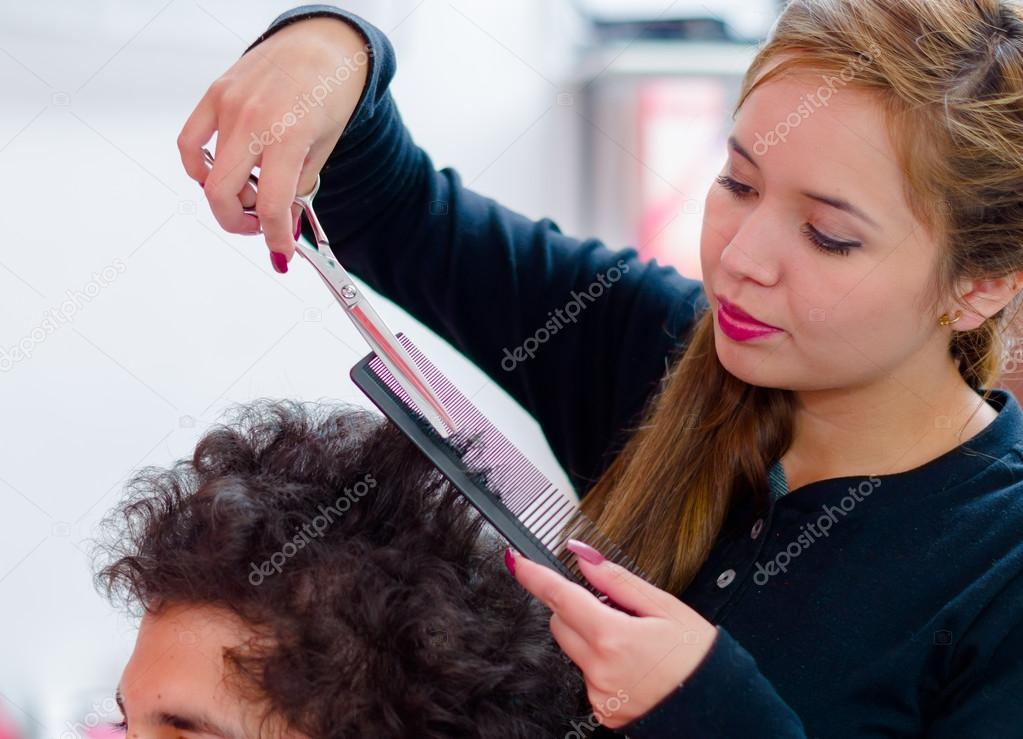 Hairstylists cutting a man curly hair, she is using a comb and scissors