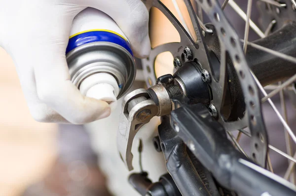 Closeup hand dragen witte handschoen met behulp van vet spray op tandrad delen van fietswiel, mechanische reparatie concept — Stockfoto