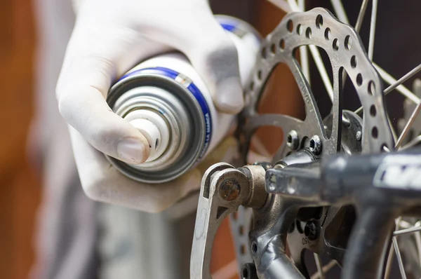 Primeros planos con guante blanco usando spray de grasa en las partes de rueda dentada de la rueda de bicicleta, concepto de reparación mecánica — Foto de Stock