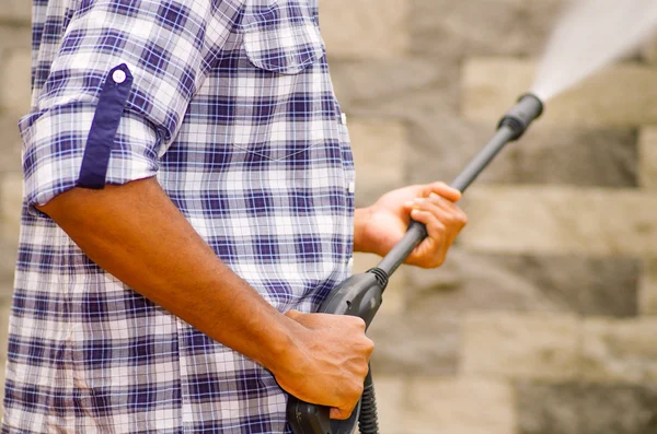 Närbild vapensköld man klädd i kvadratiskt mönster blå och vit skjorta holding högtryck vattenpistol, pekar mot grå tegelvägg — Stockfoto