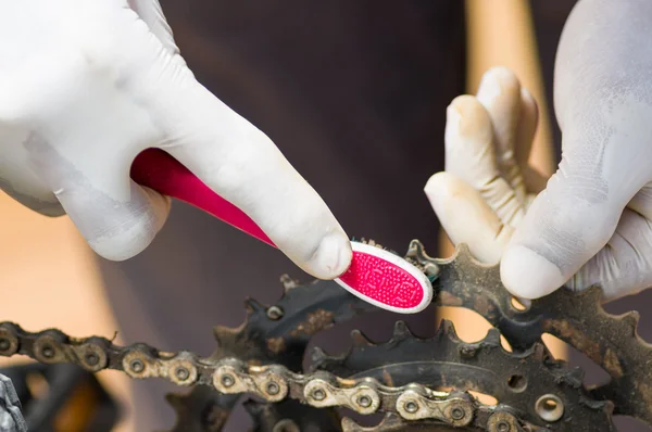 Mão de close-up usando luva branca segurando escova de dentes esfregando na cadeia de bicicleta de metal, conceito de reparo mecânico — Fotografia de Stock