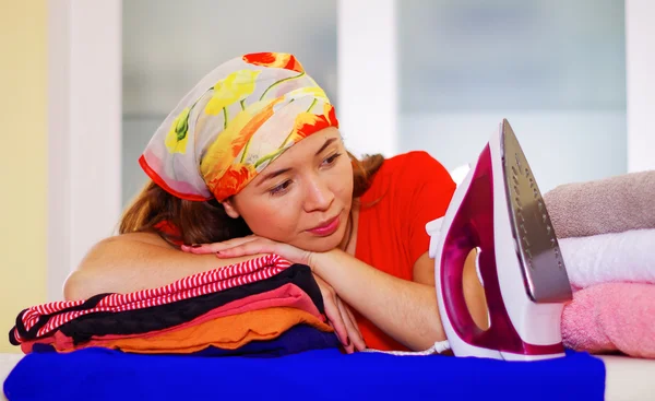 Joven encantadora mujer con colorido pañuelo de cabeza descansando cabeza en la pila de ropa, planchado concepto de tareas domésticas de lavandería — Foto de Stock