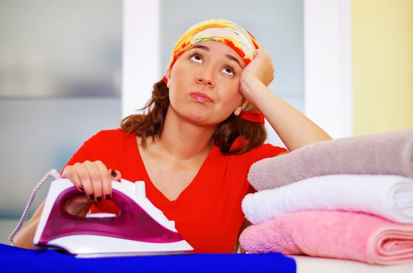 Joven mujer encantadora con colorido pañuelo para la cabeza planchar ropa mientras sueña despierto mirando en desconocido, concepto de tareas domésticas de lavandería — Foto de Stock