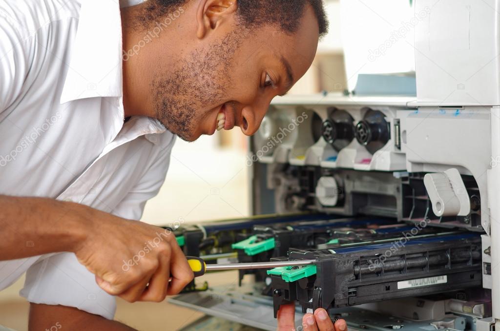 Man leaning over open photocopier during maintenance repairs using handheld tool, black mechanical parts