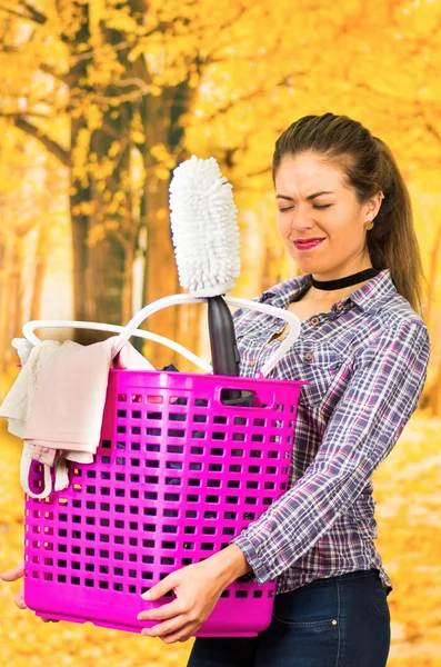 Morena atraente vestindo roupas casuais enquanto segurava cesta de plástico rosa com produtos diferentes, fechando os olhos, fundo da floresta de outono — Fotografia de Stock