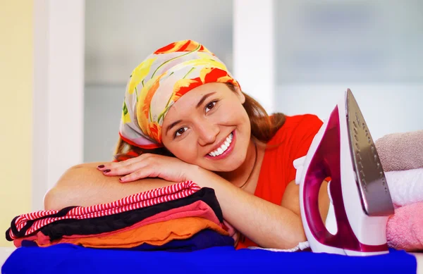 Joven encantadora mujer con colorido pañuelo de cabeza descansando cabeza en la pila de ropa, planchado concepto de tareas domésticas de lavandería — Foto de Stock