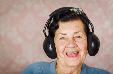 Mavi kazaklı, çiçek deseni yay ile büyük siyah etkilidirler kameraya gülümseyen pembe duvar kağıdı önünde kafasına giyen eski güzel İspanyol kadın