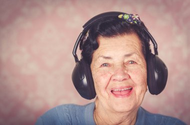 Mavi kazaklı, çiçek deseni yay ile büyük siyah etkilidirler kameraya gülümseyen pembe duvar kağıdı önünde kafasına giyen eski güzel İspanyol kadın