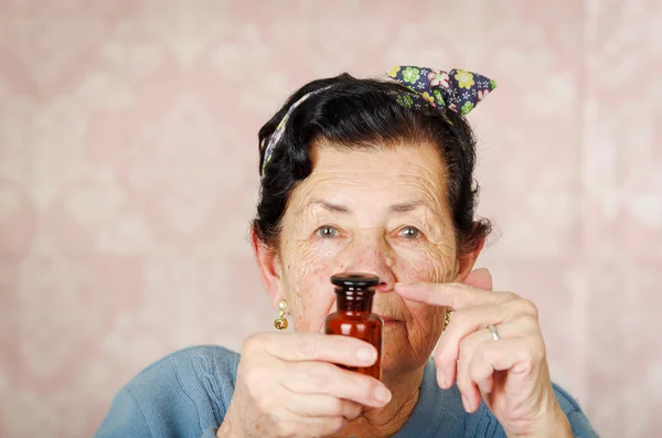 Femme hispanique cool plus âgée portant un pull bleu, motif de fleurs arc sur la tête tenant une petite bouteille en verre rouge pour appareil photo — Photo