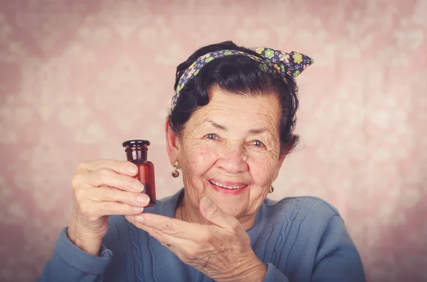 Starší cool hispánský žena na sobě modrý svetr, květinový vzor bow na hlavě drží malé červené skleněné láhve a úsměv do kamery — Stock fotografie
