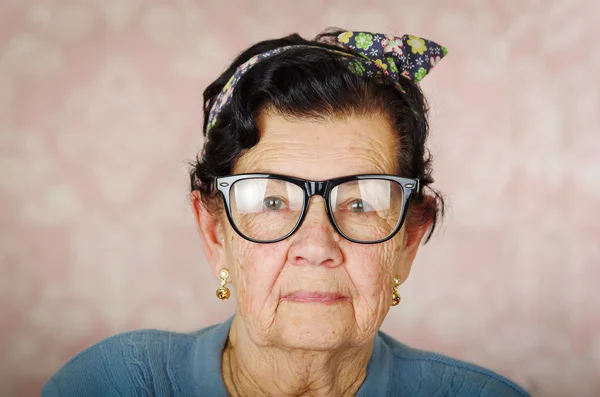 Oudere hispanic leuke vrouw met bloem patroon strik op haar hoofd droeg blauwe trui en zwarte grote ingelijste bril op zoek naar camera — Stockfoto