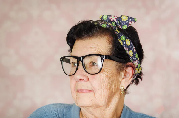 Ancienne hispanique mignonne femme avec motif fleur arc sur sa tête portant pull bleu et noir grandes lunettes encadrées regardant vers le côté de la caméra — Photo