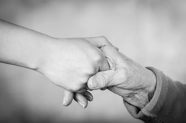 Gros plan deux mains se tenant l'une l'autre semblant être celle d'un jeune et d'une personne âgée en édition noir blanc — Photo