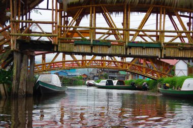 Pasto, Kolombiya - 3 Temmuz 2016: La Cocha Gölü'ne yakın bir nehirde iki köprünün altına park edilmiş bazı yeşil tekneler