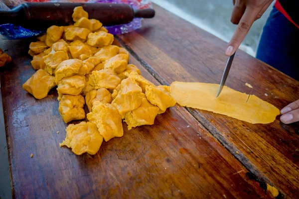 Alguém cortando um amarelo pronto áspero em uma mesa de madeira — Fotografia de Stock