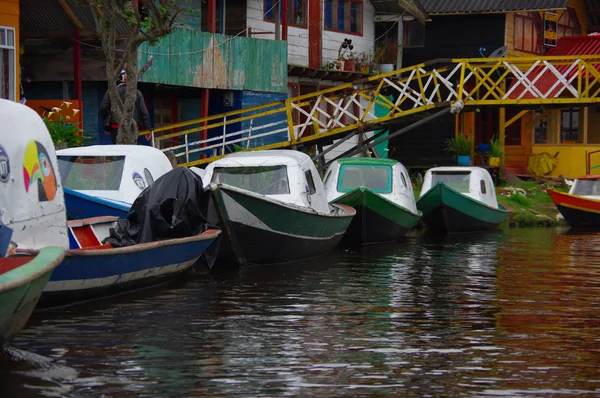 Pasto, kolumbien - 3. juli 2016: einige bunte boote, die am ufer neben einigen häusern und unter einer kleinen brücke im la cocha see geparkt sind — Stockfoto