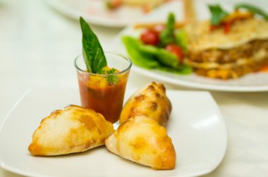 Apetizer shotglass ve lezzetli mini empanadas etrafında beyaz plaka üzerinde yayılmış küçük domates çorbası